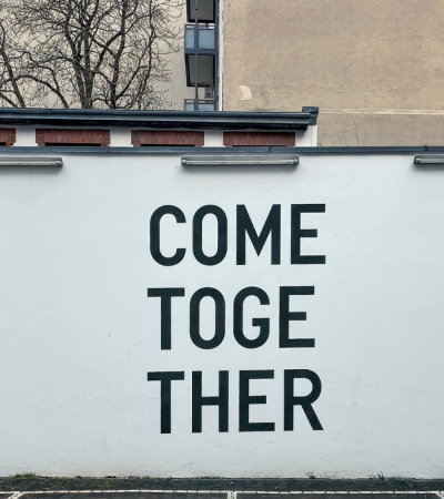 Photograph of a white wall with black letters spelling Come Together