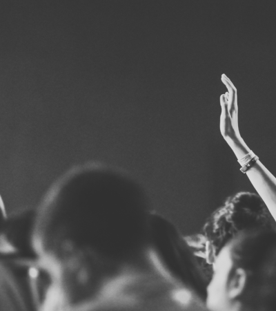 Black and white photograph shows a crowd of people. There is a person raising their hand in the crowd.