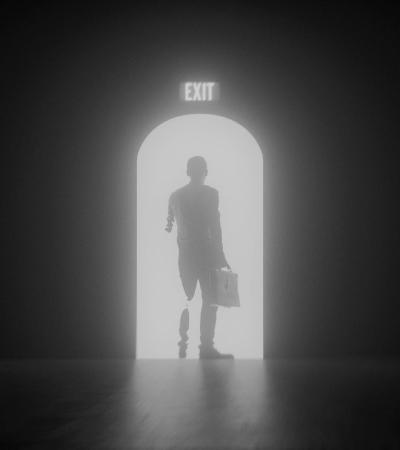 Black and white photograph of person holding a brief case exiting a dark room into brightness.