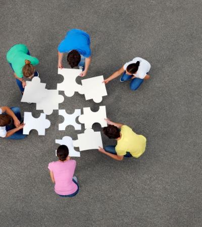 Aerial photograph of six people putting together a large jigsaw puzzle.