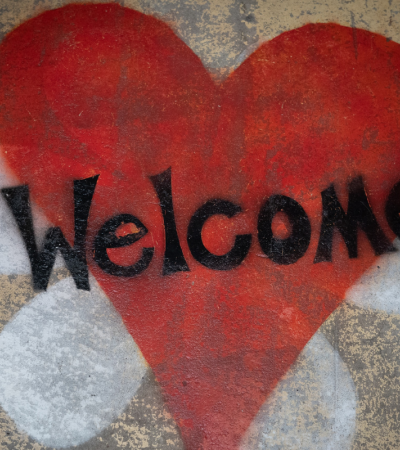 Photograph of a street art. The word welcome is written in black across a red heart.