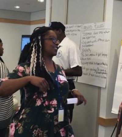 Man and woman stand to the side of a conference room talking.