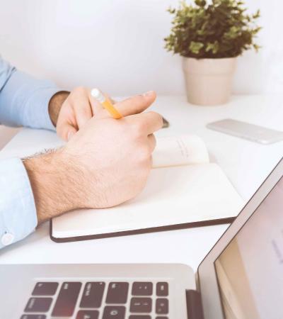 Man writing in journal next to laptop