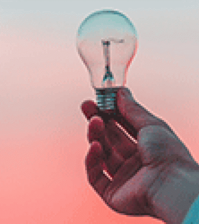 Hand holding a lightbulb against a pink and blue sky