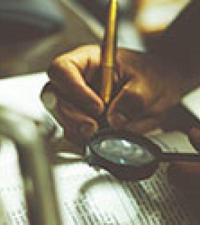 Person holding magnifying glass and taking notes in a book