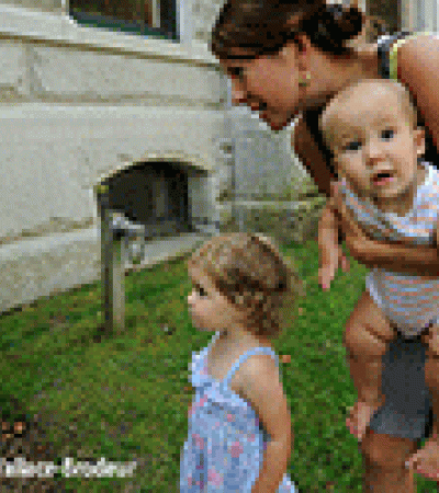 A woman holding a baby and reading a StoryWalk post with a toddler