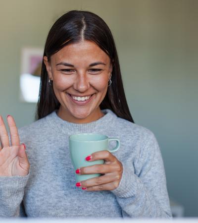 A woman holding a coffee cup smiling at a computer screen