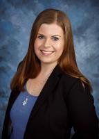 woman with long brown hair smiling at camera wearing a blue shirt and black blazer