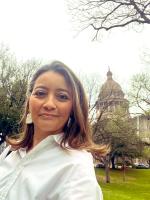 a woman with medium length hair wearing a white blouse and earrings stands in a park in front of a government building