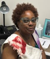 woman with brown curly hair and glasses smiling for camera wearing white and red shirt