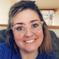 Smiling woman with brown hair and glasses wearing a blue shirt.