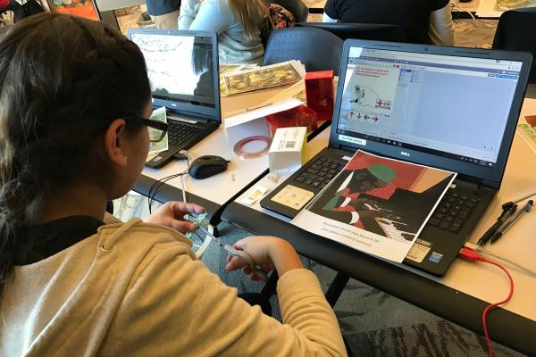 Photograph of a teen working on creating a tactile book, they are cutting out designs in front of an open laptop.