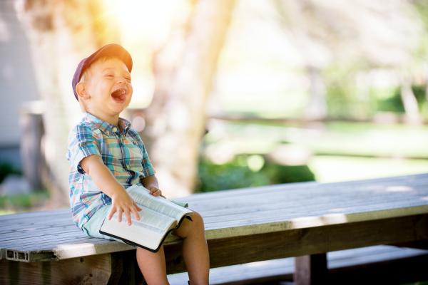 Photograph of smiling child sitting on a bench holding an open book