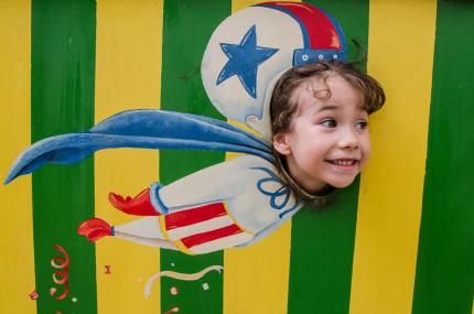 little girl pretending to fly like a cannon ball out of a cannon using a face-cutout at a circus