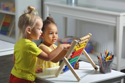 preschool girls of different ethnicities sit together at table counting on abacus