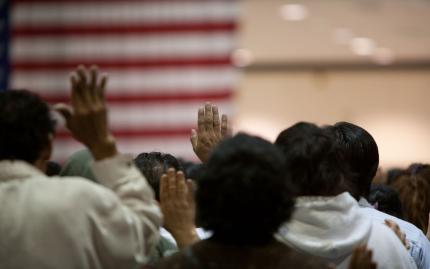 Photograph shows people at a swearing in ceremony for US citizenship.