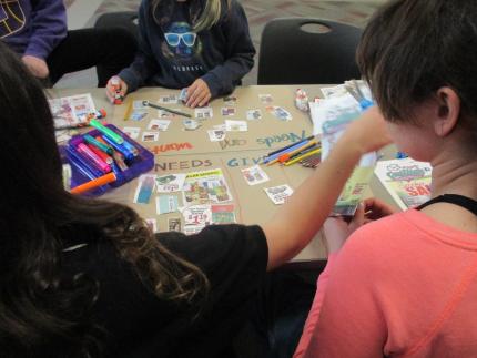 Photograph of kids working at a table with art supplies to create their Needs and Wants project