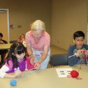 Student getting help from teacher with a another student knitting