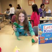 Student posing with her knitting project and a Let's Knit book