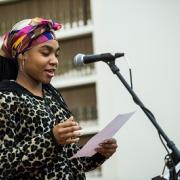 Woman at microphone reading poem at the Traveling Stanzas opening reception