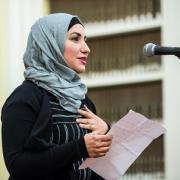 Woman at microphone reading poem at the Traveling Stanzas opening reception