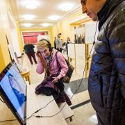 Two people listening to headphones and watching screens at the opening reception