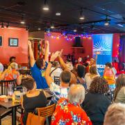 Photograph of a large trivia group celebrating a win with their aims up in the air