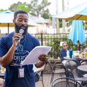 Photograph of a person speaking into a microphone at an outdoor event