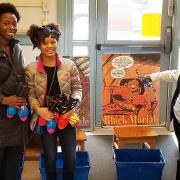 Three people stand and smile in front of superhero poster