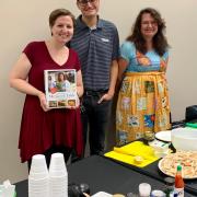 Three people standing behind a table with food to prepare