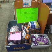 Photograph of materials donated to local animal drive. There is a green sign that reads Animal Drive. Boxes contain dog and cat food and other supplies.