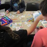 Photograph of kids working at a table with art supplies to create their Needs and Wants project