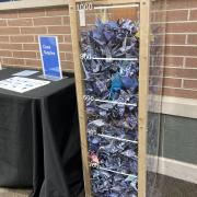 Photograph shows a clear box full of finished paper cranes. The cranes fill the box up to the 1000 mark.