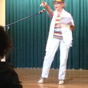 A woman stands in front of an audience and performs her memoir on stage.