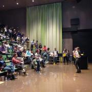 A woman addresses a large auditorium filled with people.