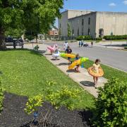 Photograph shows children outside playing a sidewalk chalk game with pool floaties on.