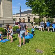 Photograph shows a group of people outside of the library building playing outdoor games.