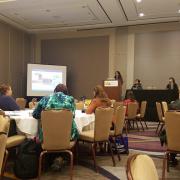 A woman gives a presentation to a crowded room.