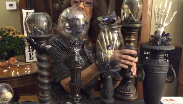 Photograph of five completed Crystal Ball Candlesticks. They have black bases and glass balls with skeleton hand decorations.