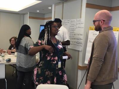 Man and woman stand to the side of a conference room talking.