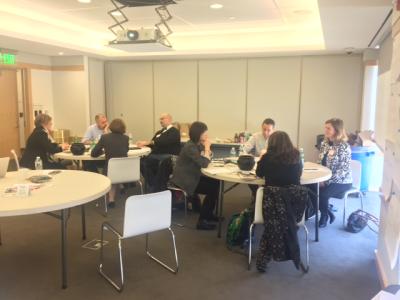 Two groups of people sit at two tables and participate in a meeting.