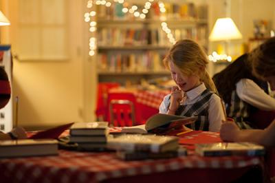 Little girl reading a book at a cafe table